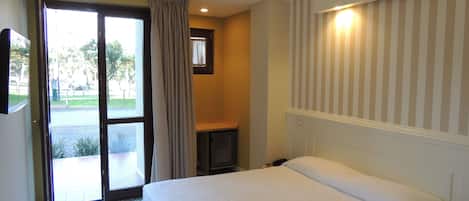 A hotel room with a bed, a small table, a chair, a window with curtains, and a view of the outside.