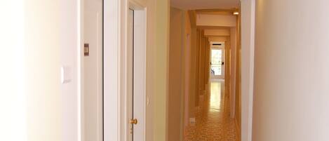 A narrow hallway with patterned floor tiles, white walls, and a series of doors on the left.