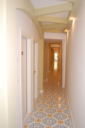 A narrow hallway with patterned floor tiles, white walls, and a series of doors on the left.