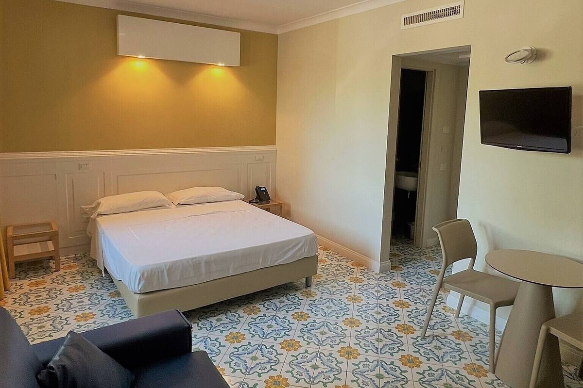 Una habitación de hotel con cama, escritorio, silla y televisión en la pared.