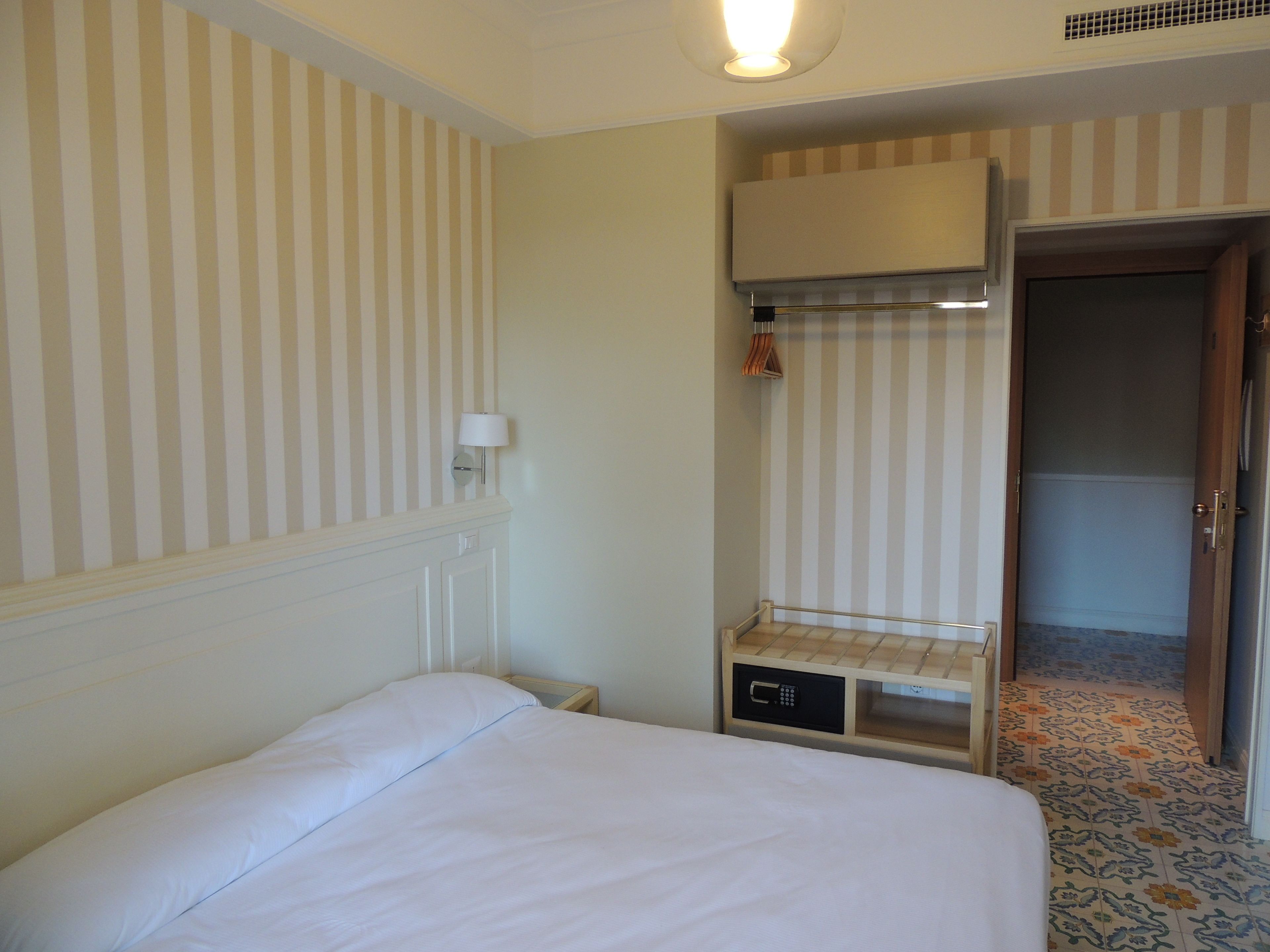 Una habitación de hotel con cama, mesita de noche, lámpara y armario.