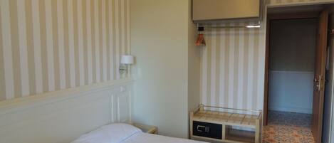 A hotel room with a bed, a small bedside table, a lamp, and a wardrobe.