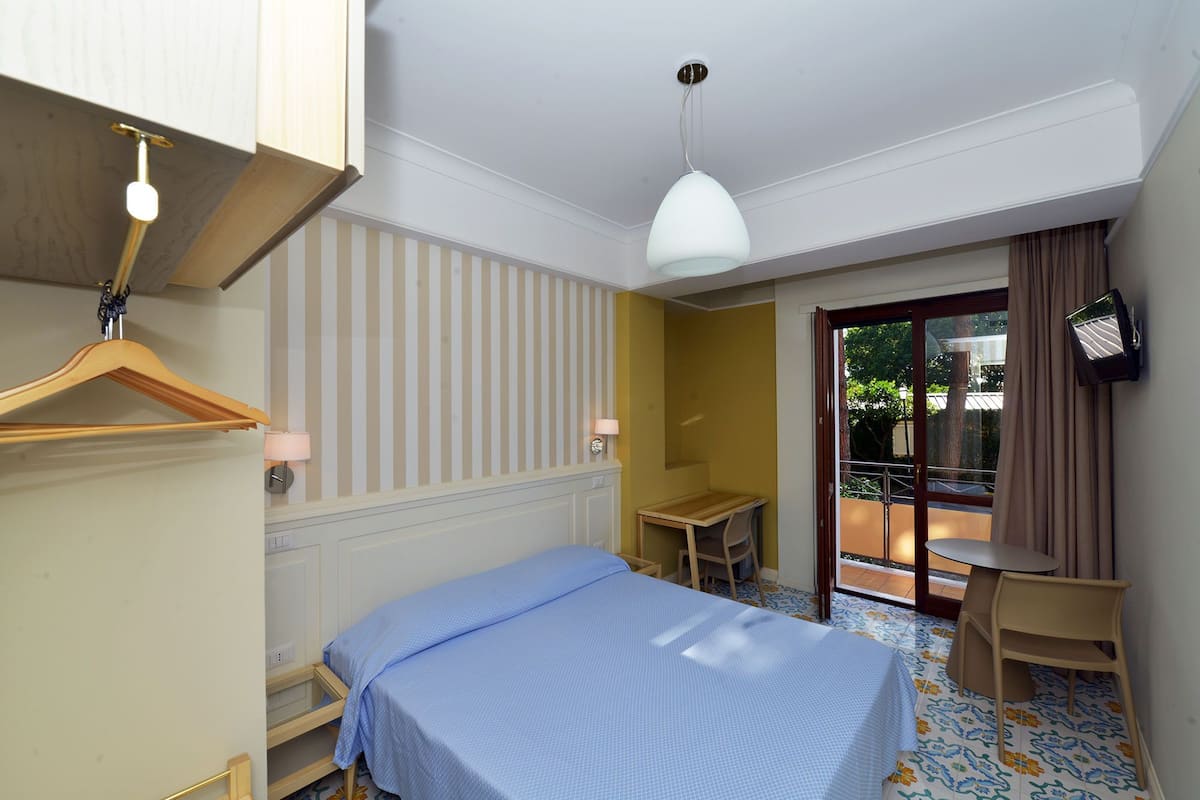 Habitación de hotel con cama, escritorio, silla, lámpara colgante y televisor en la pared.