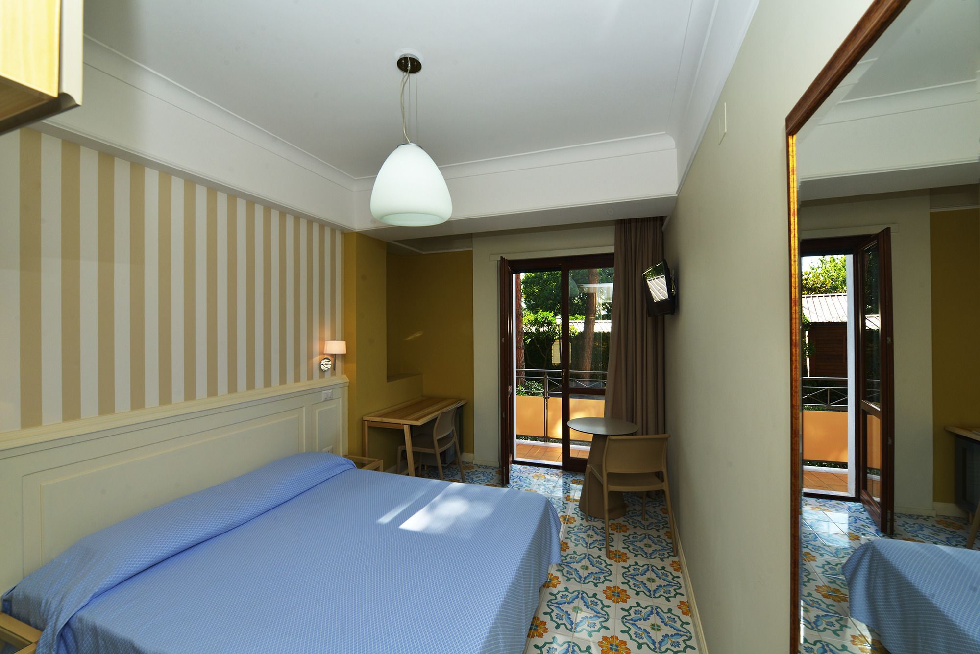Habitación de hotel con cama, escritorio, silla y balcón con vistas.