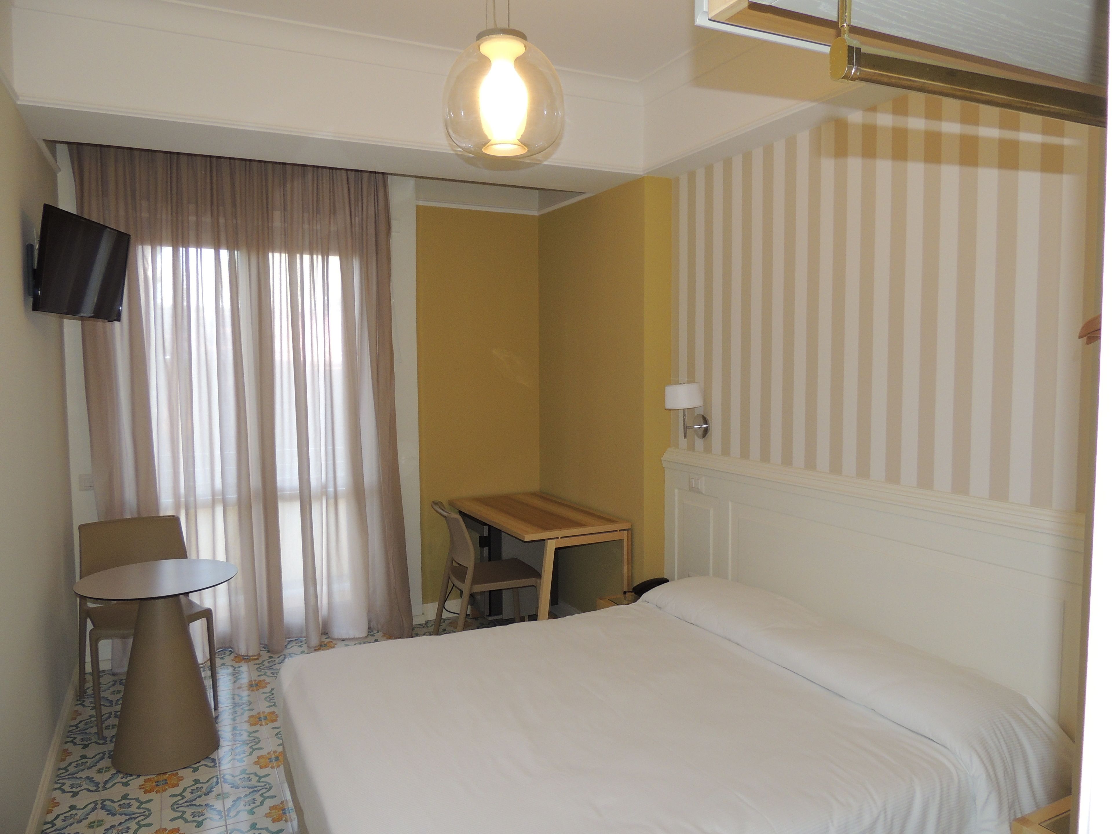 A hotel room with a bed, a desk, a chair, a TV, and curtains.