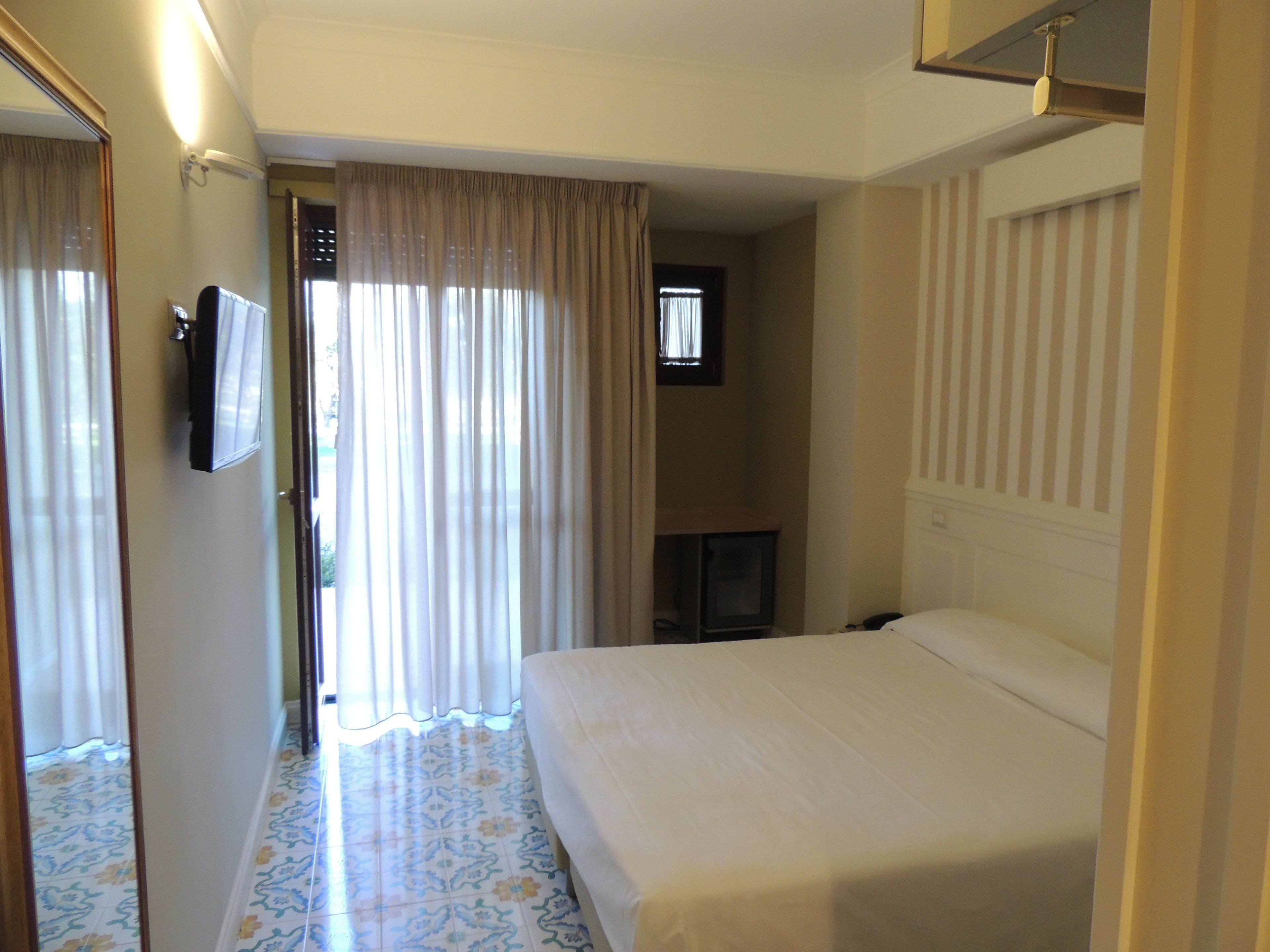Una camera d'albergo con un letto, una televisione, uno specchio e una porta che dà su un'altra stanza.