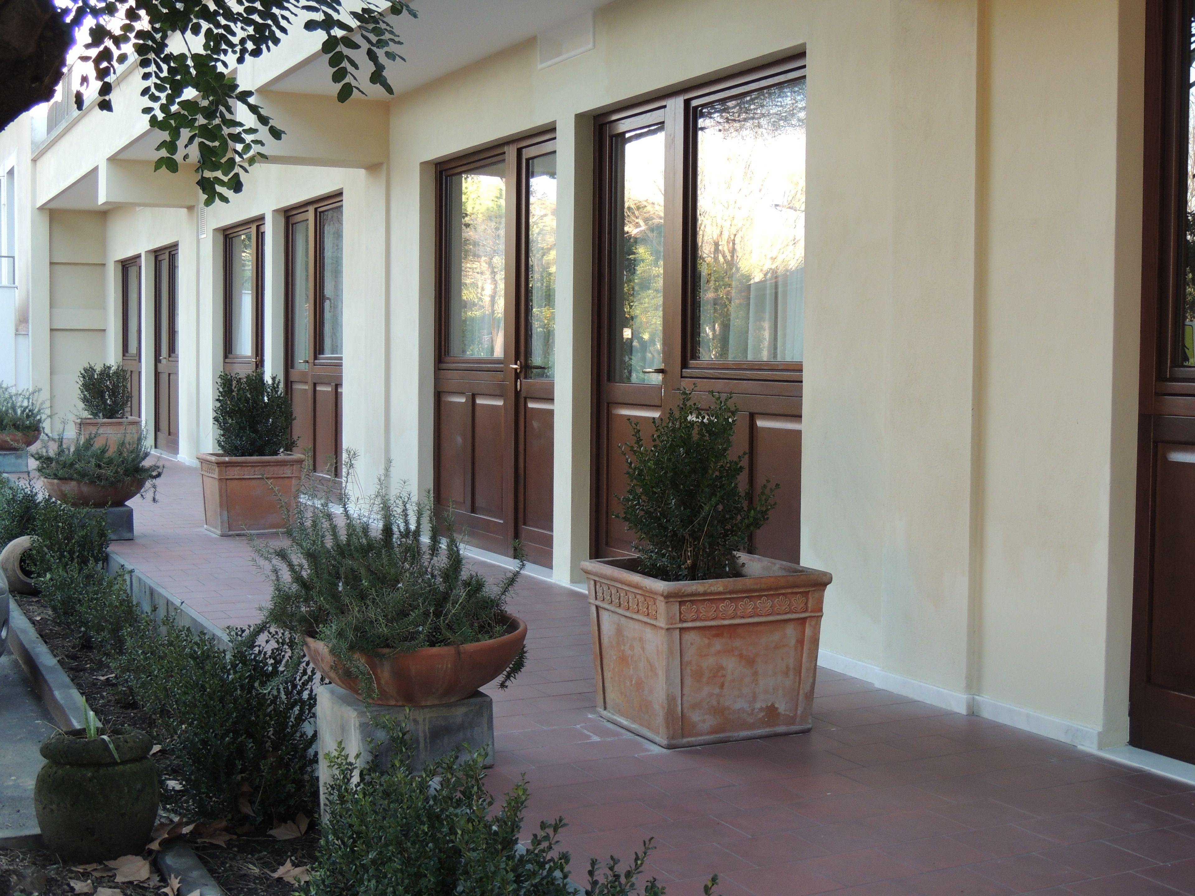 A covered walkway with large windows, potted plants, and a tiled floor.