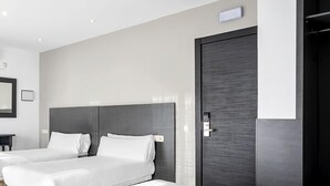 A hotel room with two single beds, a dark wooden door, and a small bedside table. - Hotel Victoria Valdemoro  (Valdemoro)