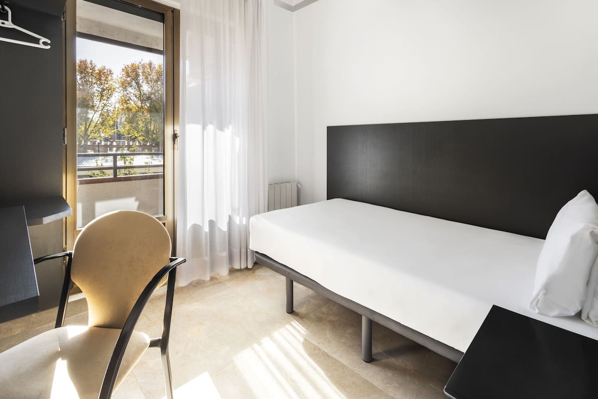 Una habitación de hotel con una cama, una silla, un escritorio y una ventana con cortinas.