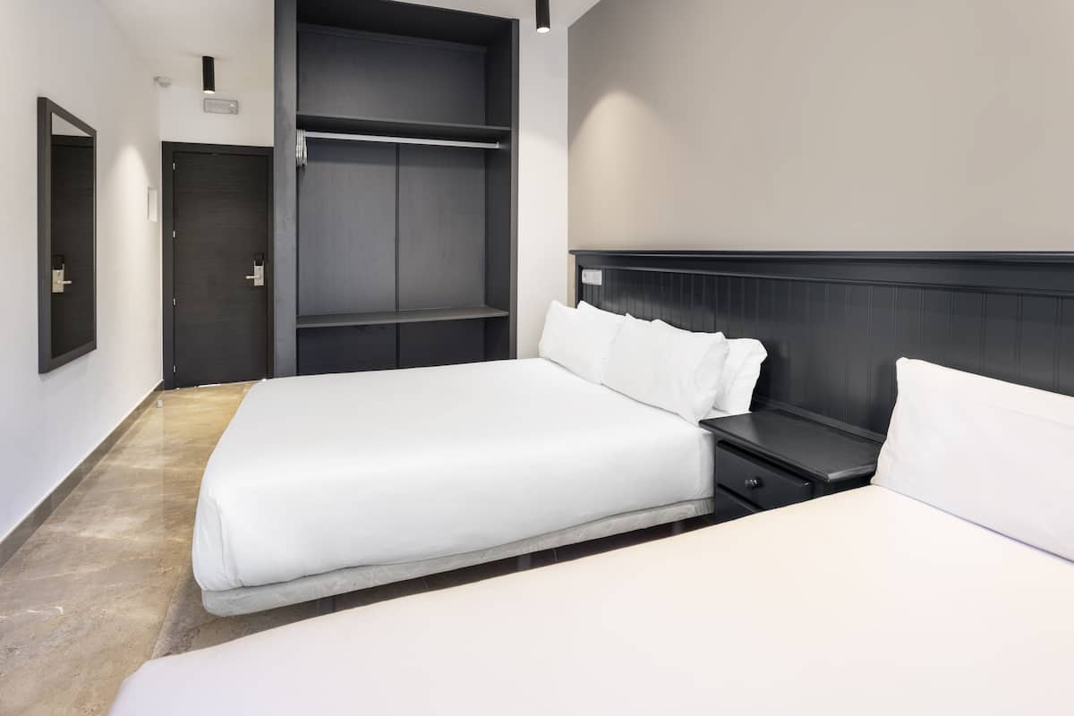 Una habitación de hotel moderna con una cama grande, una mesita de noche, un armario y un espejo.
