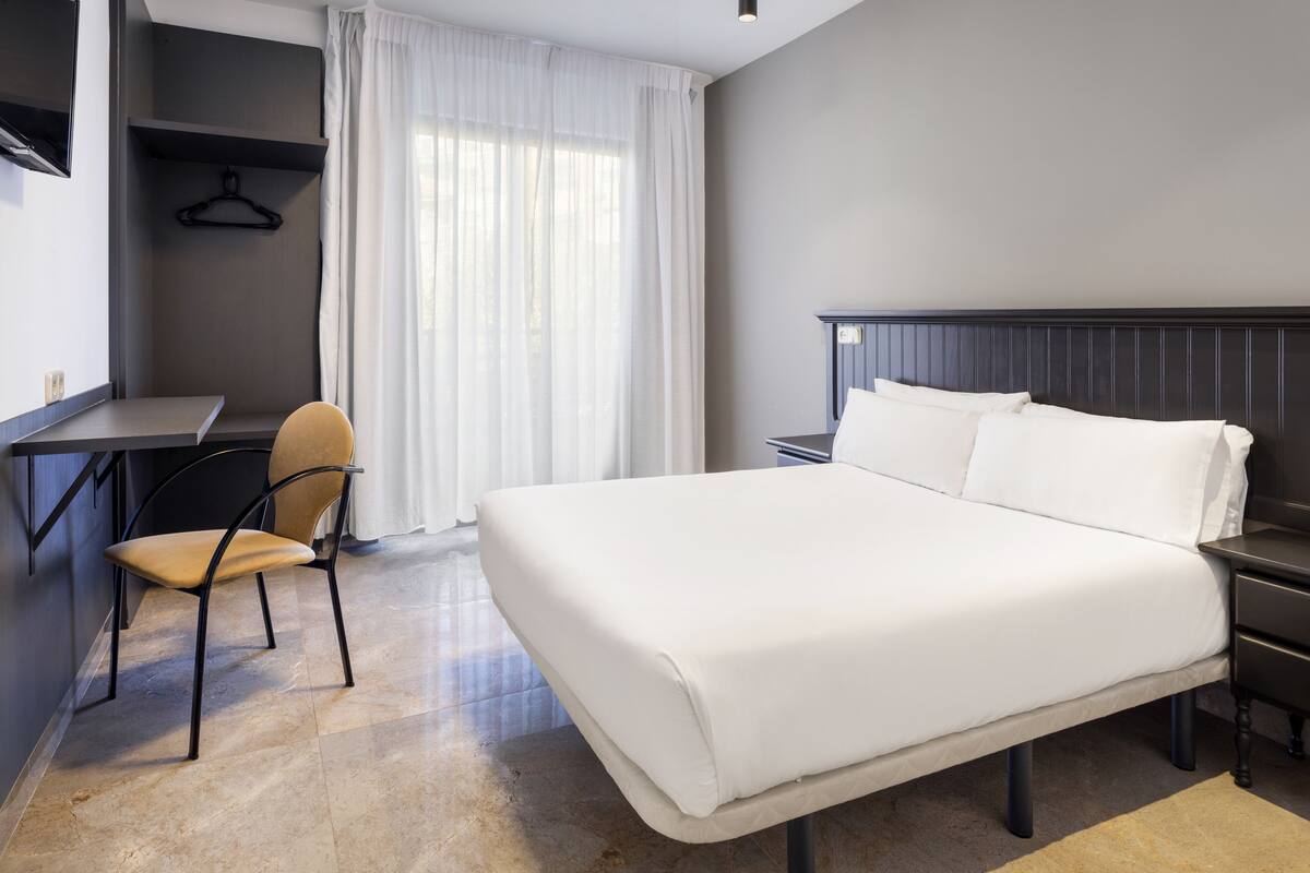 Una habitación de hotel con cama, escritorio, silla y televisor montado en la pared.