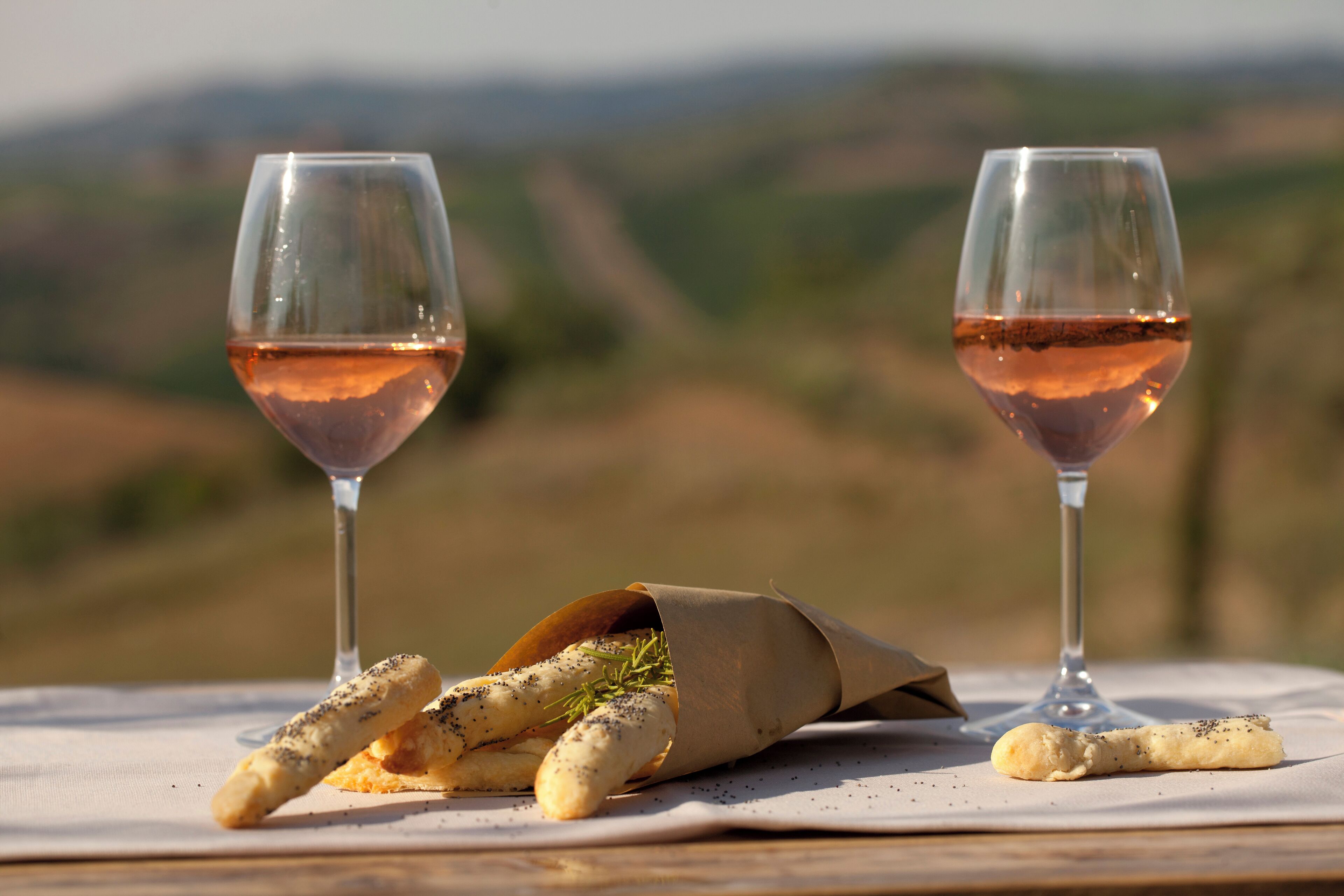 Two glasses of rosé wine on a table with a napkin and breadsticks.