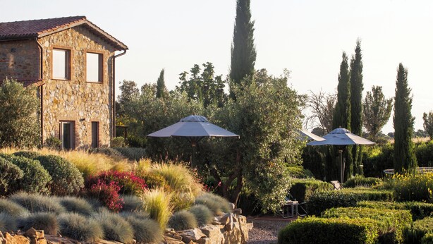 A stone house with two windows and a patio area with two umbrellas. - Casale Sterpeti (Magliano in Toscana)