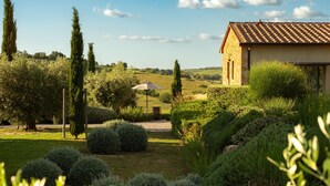 A rustic stone building with a tiled roof, surrounded by well-maintained gardens and tall trees. - Casale Sterpeti (Magliano in Toscana)
