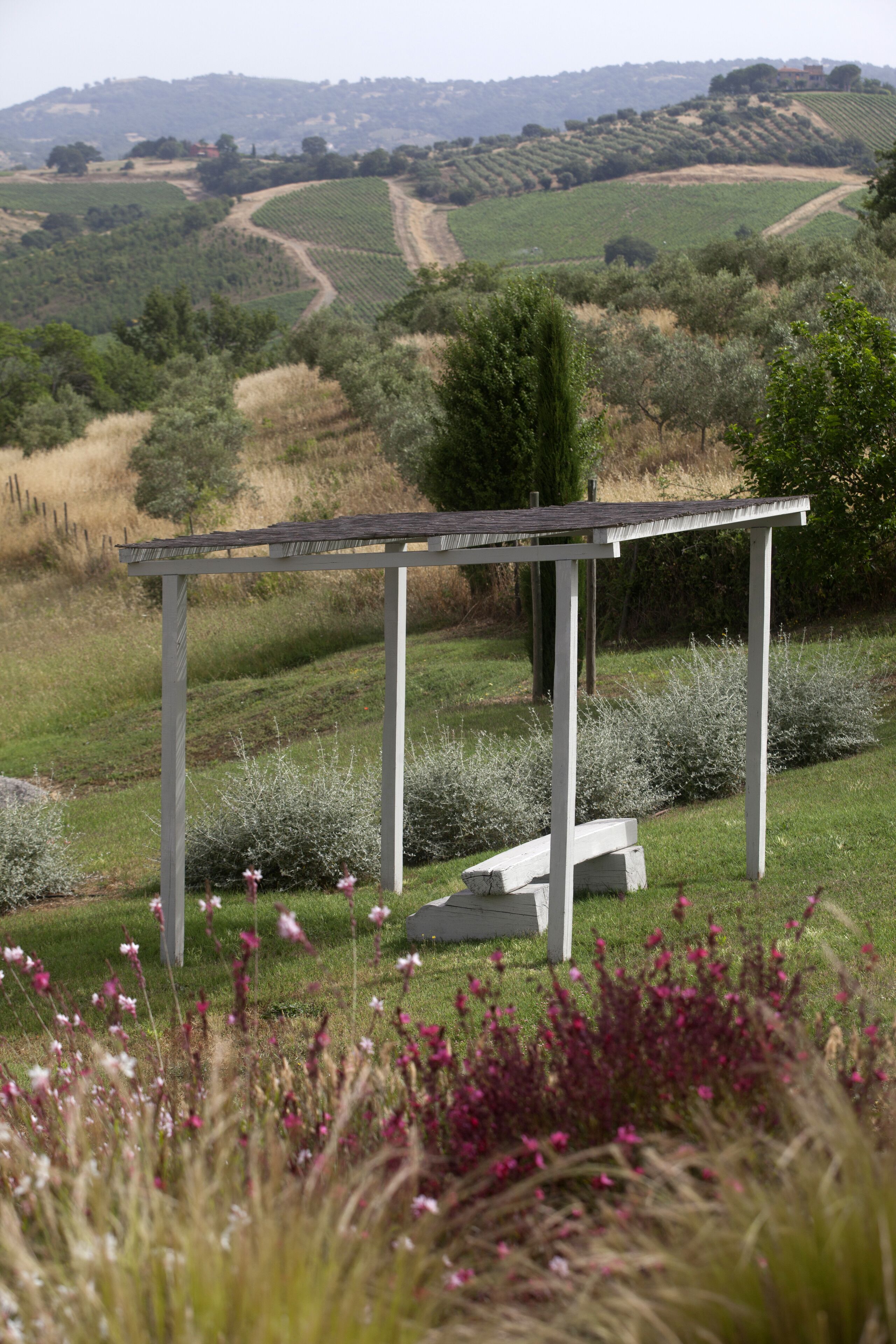 Een witte pergola met een bank in een grasveld, met uitzicht op glooiende heuvels.