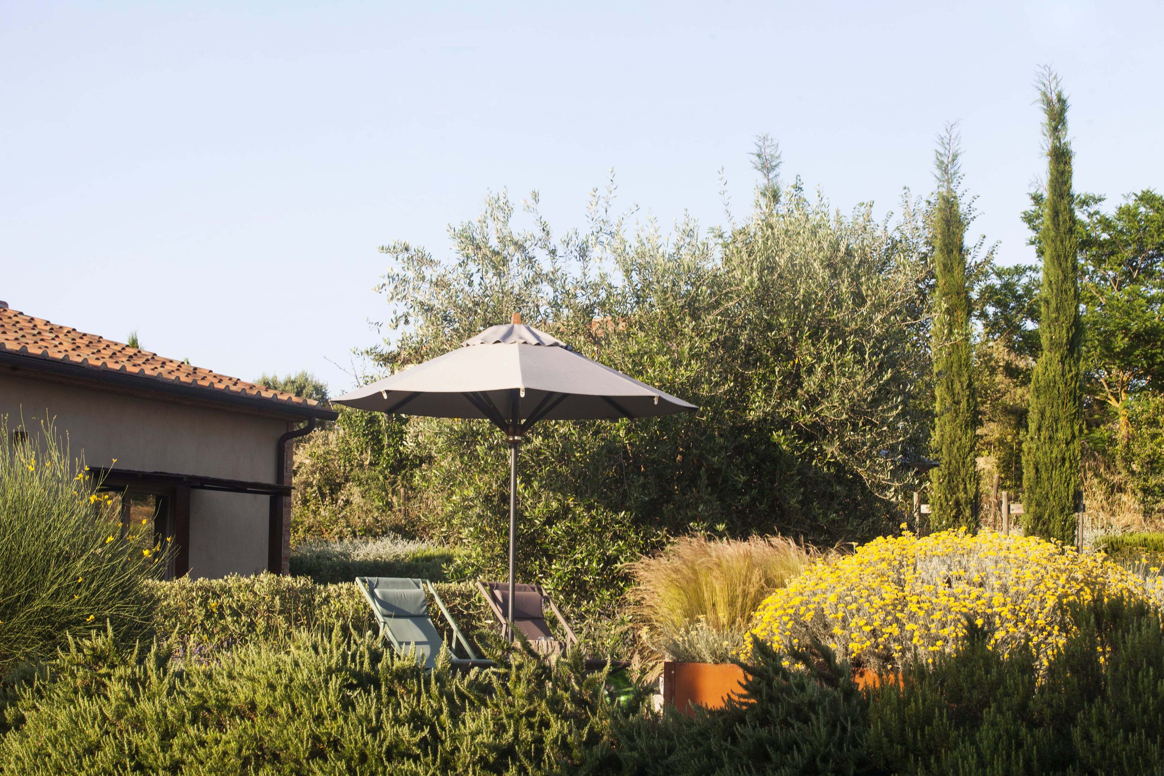 Um jardim com um pátio, incluindo uma mesa, cadeiras e um guarda-sol.