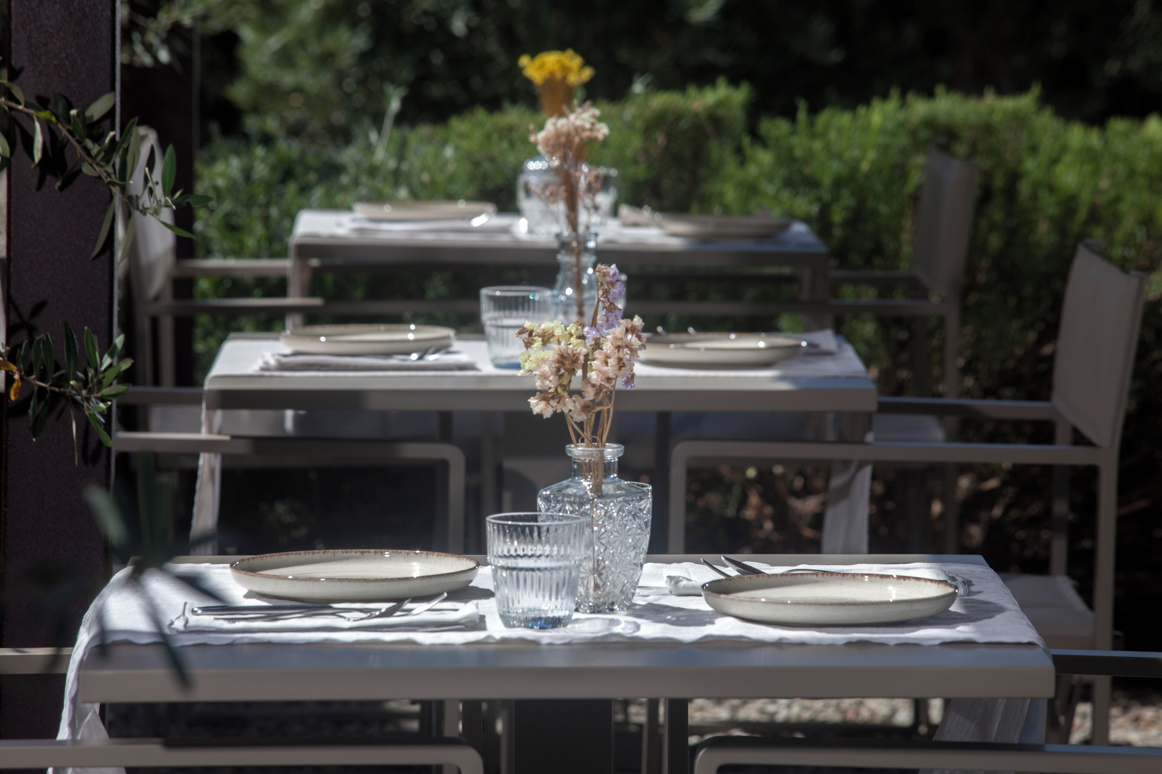 Una mesa al aire libre con platos, vasos y un jarrón de flores.
