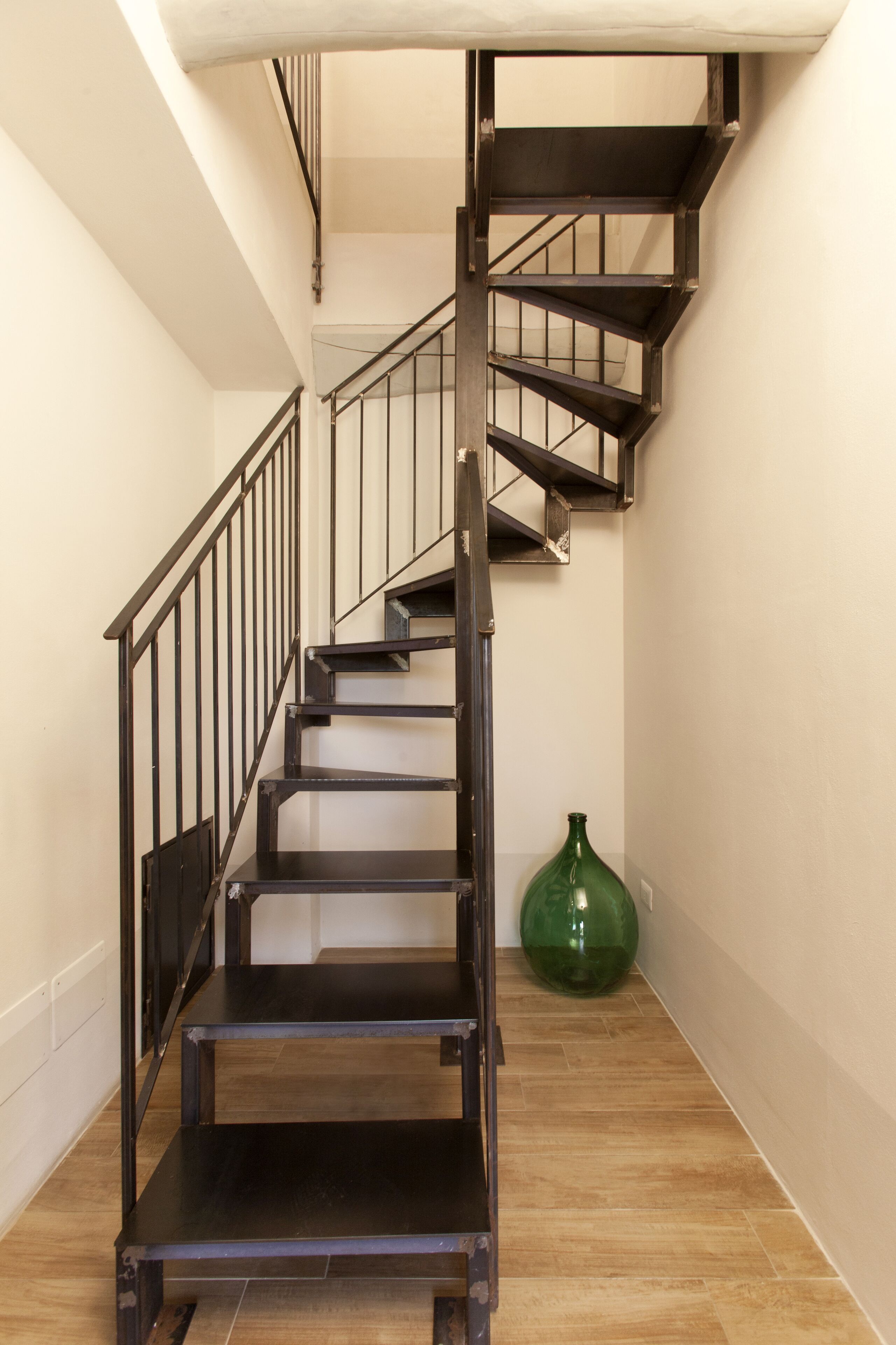 A staircase with a metal railing and a green vase on the floor.