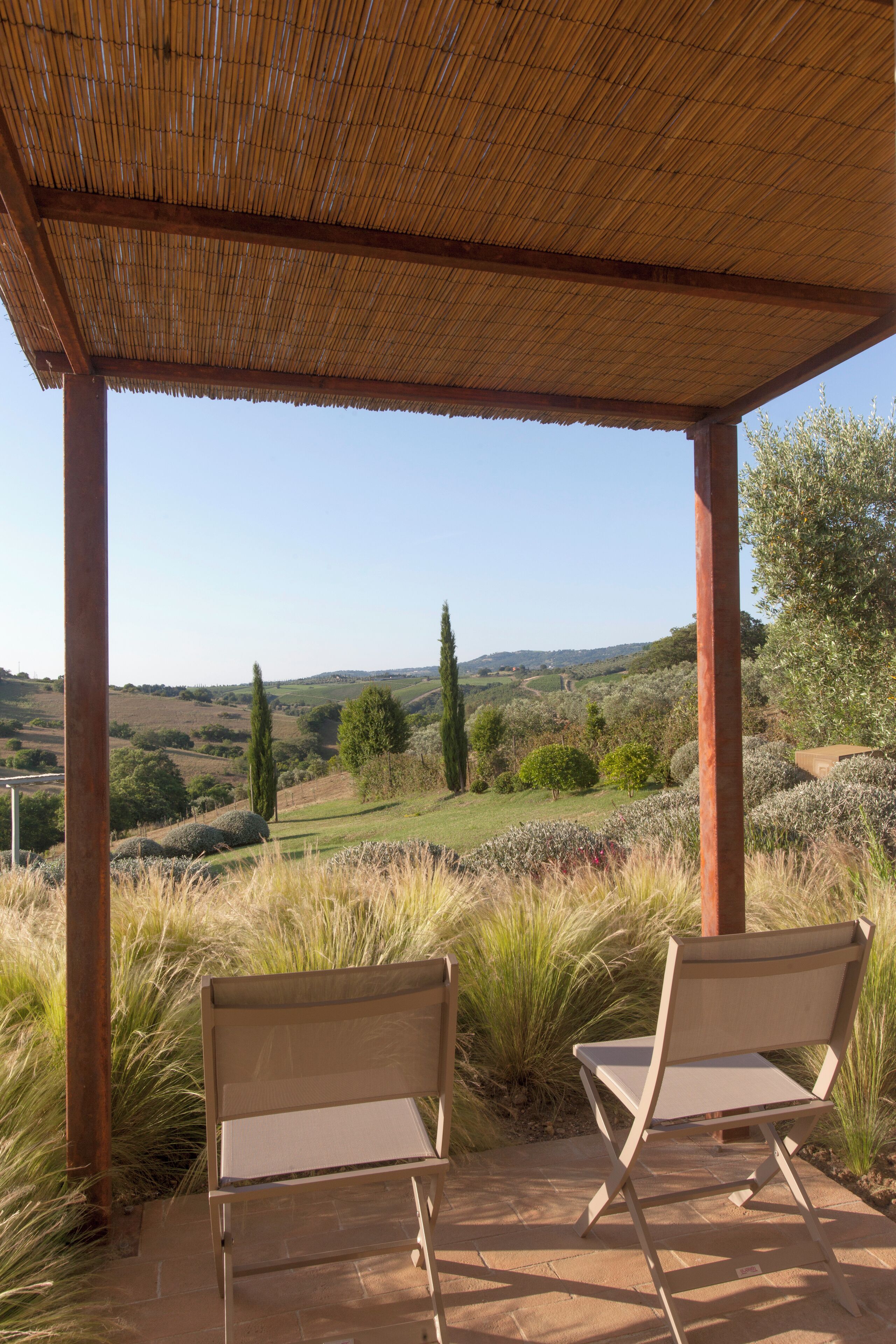 Un espace extérieur aménagé avec deux chaises, protégé par un toit, et offrant une vue panoramique sur un paysage pittoresque composé de collines douces et d’arbres.