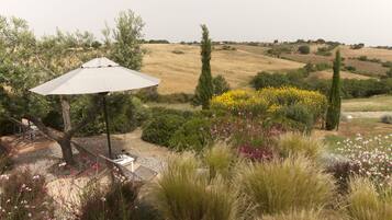 A garden with a white umbrella, a bench, and a view of rolling hills.