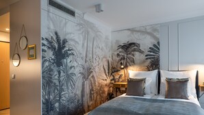 Un dormitorio con un gran mural de follaje tropical en la pared, una cama con colcha estampada y una mesita de noche con una lámpara.