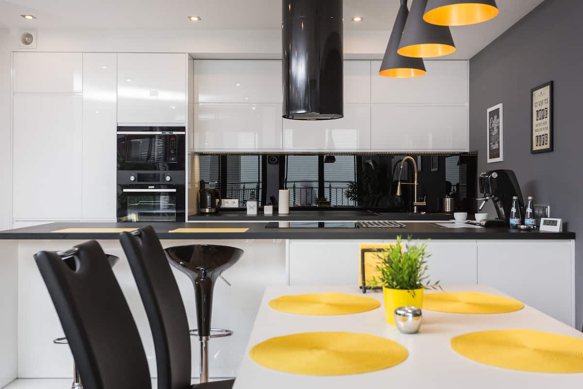 A modern kitchen with white cabinets, a black countertop, and yellow placemats on the dining table.