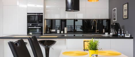 A modern kitchen with white cabinets, a black countertop, and yellow placemats on the dining table.