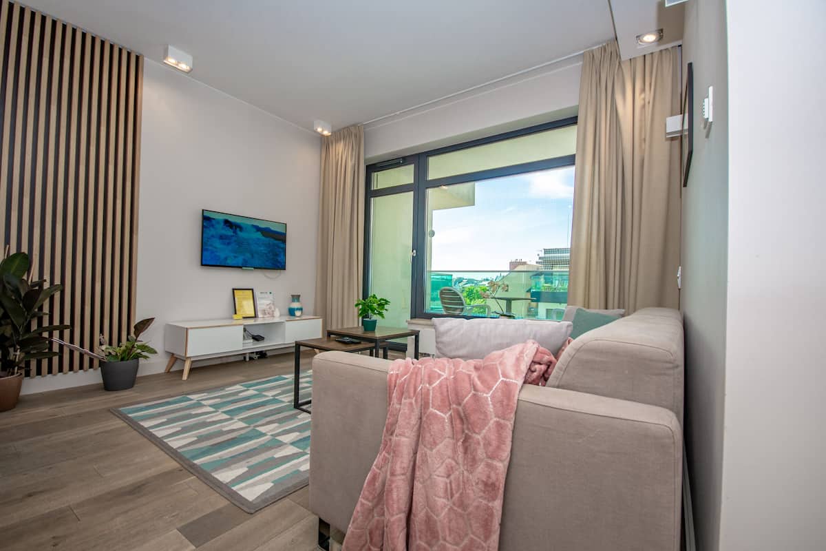 A modern living room with a sofa, a TV, a plant, and a view of the city.