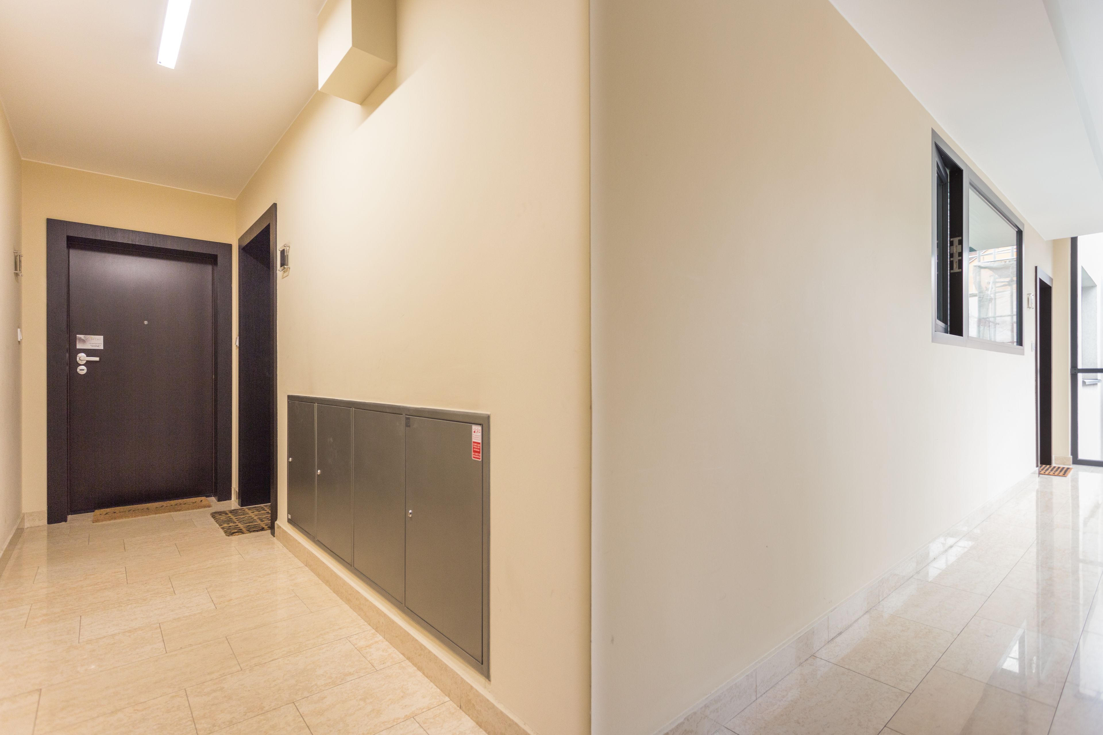 A hallway with a dark door, a set of lockers, and a window on the right.