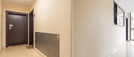 A hallway with a dark door, a set of lockers, and a window on the right.