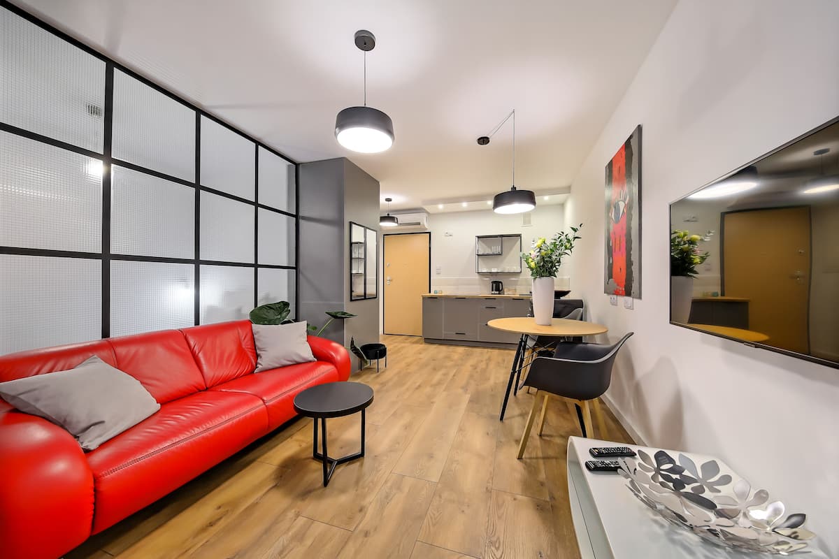 A modern living room with a red sofa, a small round table, and a dining area with a black chair.