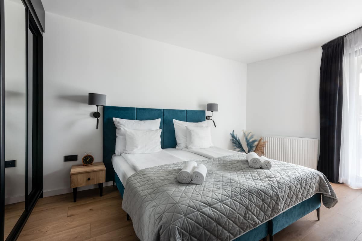 A modern bedroom with a large bed, two bedside lamps, a nightstand, and a window with curtains.