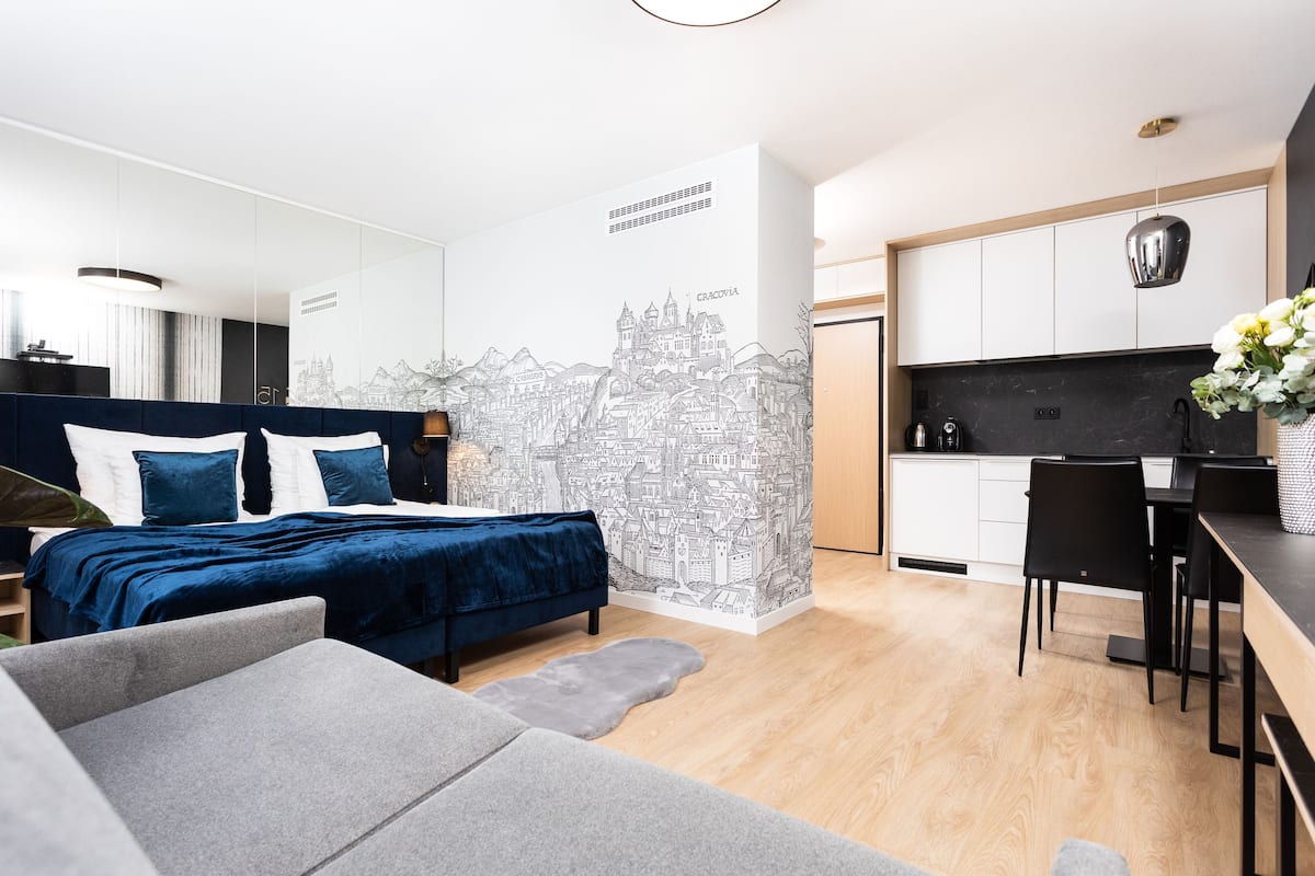 A modern bedroom with a bed, a grey sofa, a small rug, and a wall mural.