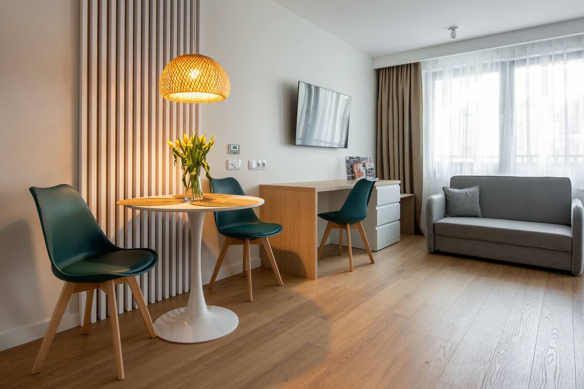 A modern hotel room with a dining area, a sofa, and a TV on the wall.