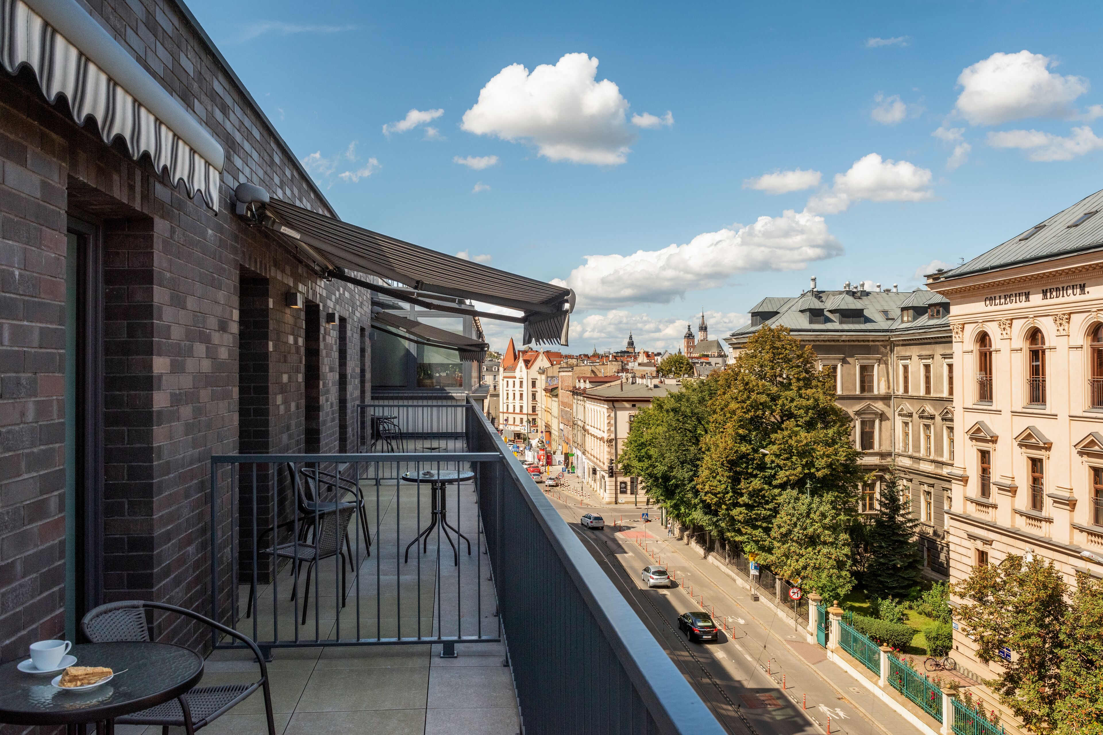 A balcony with a table and chairs, overlooking a street with historic buildings and a clear sky.