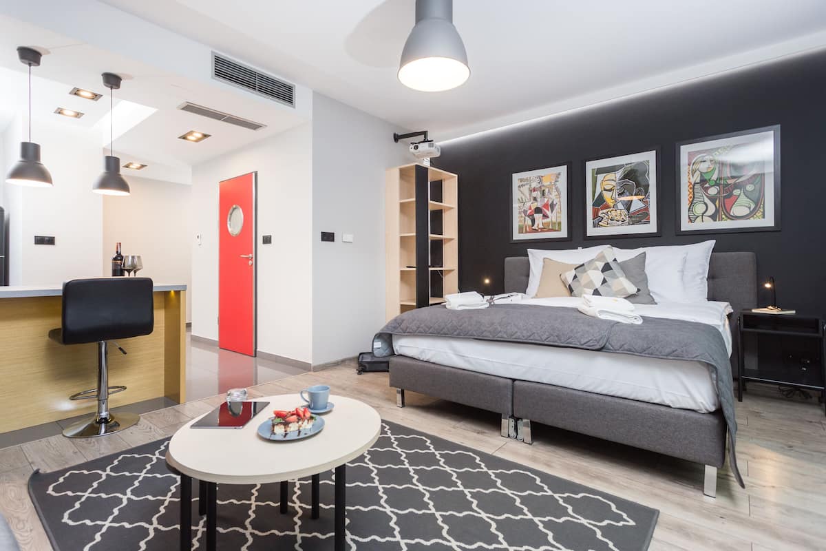 A modern hotel room with a bed, bedside table, and a small dining area.