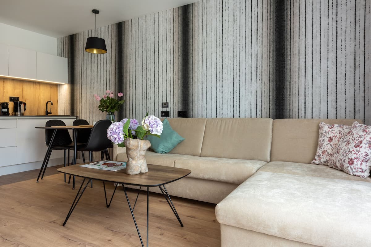 A modern living room with a sofa, a coffee table, and a dining area with chairs and a kitchen in the background.