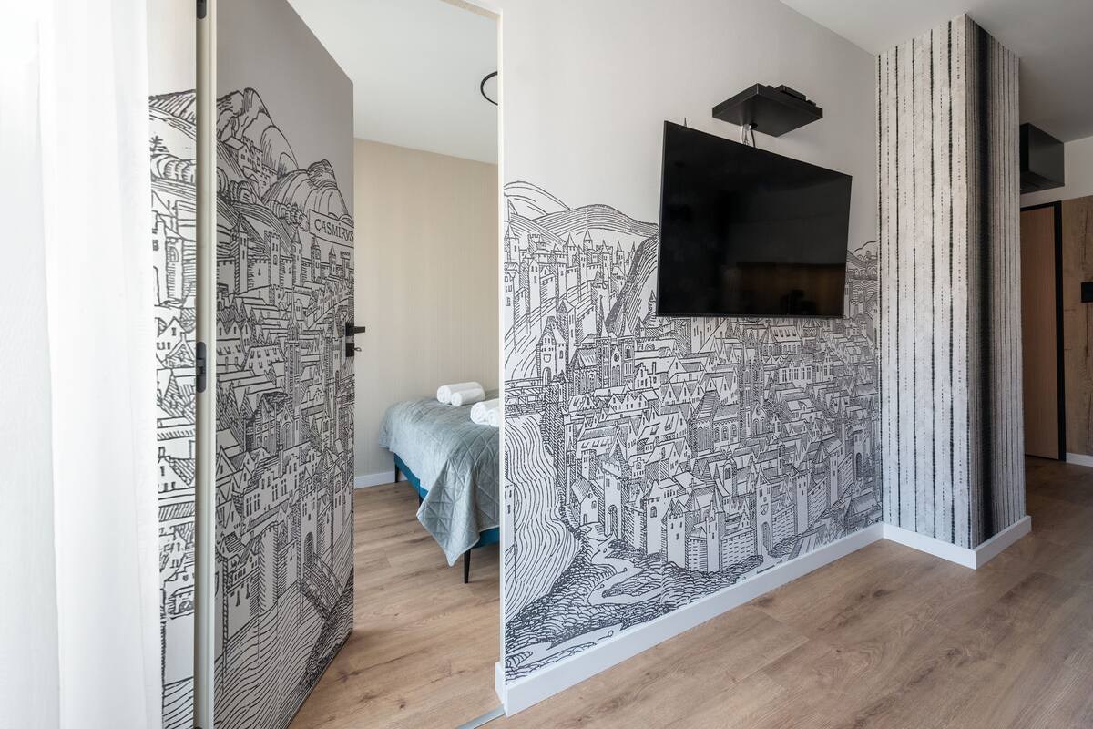 A bedroom with a bed, a TV mounted on the wall, and a large black and white mural.