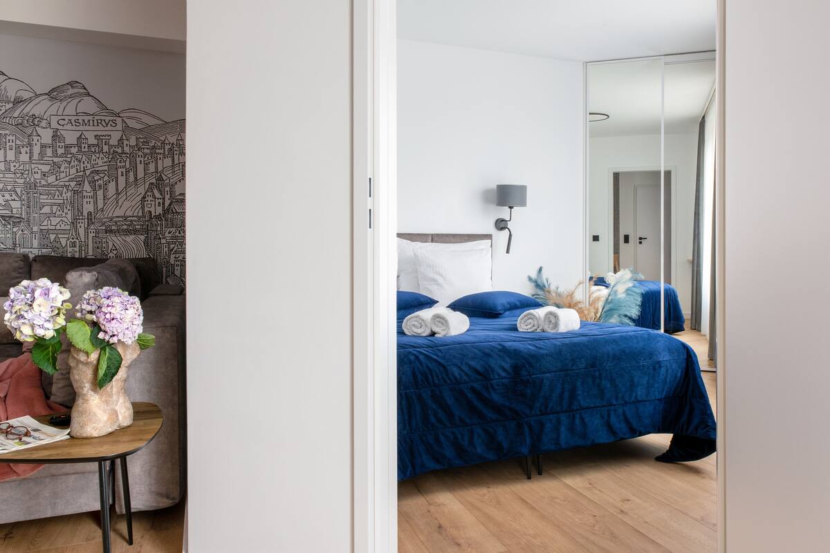 A bedroom with a blue bedspread, white pillows, and a nightstand with a lamp.