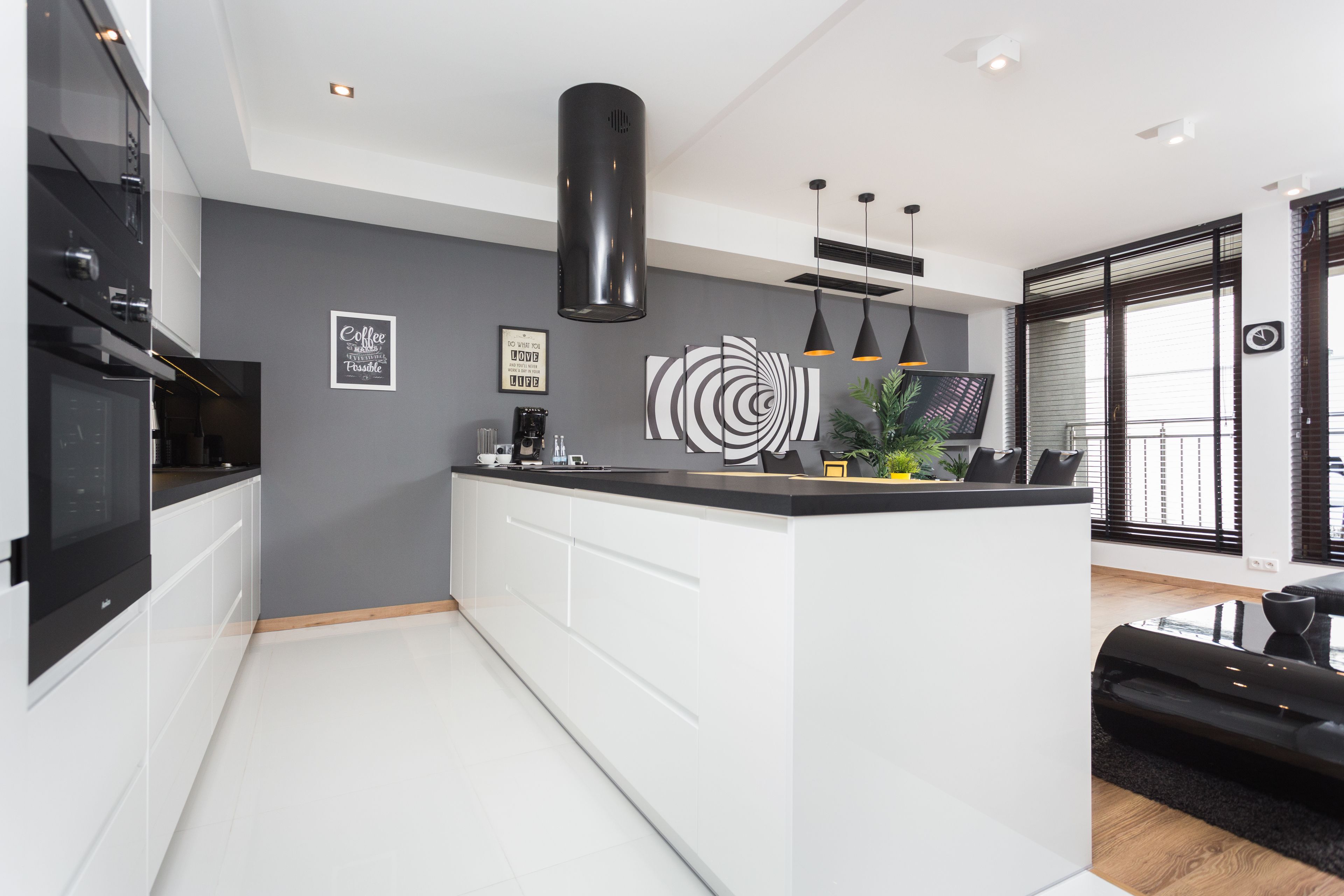 A modern kitchen with a central island, black pendant lights, and a grey accent wall with a circular design.