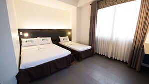 Une chambre d’hôtel avec deux lits simples, une tête de lit, une fenêtre avec des rideaux et un sol recouvert de moquette.