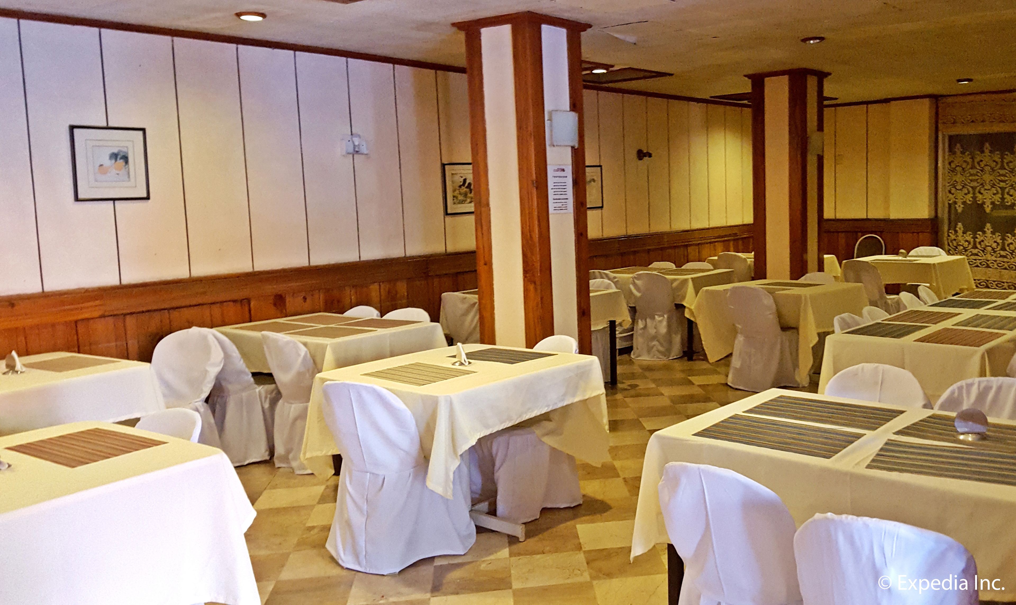 A banquet hall with multiple tables covered in white tablecloths, arranged in rows.