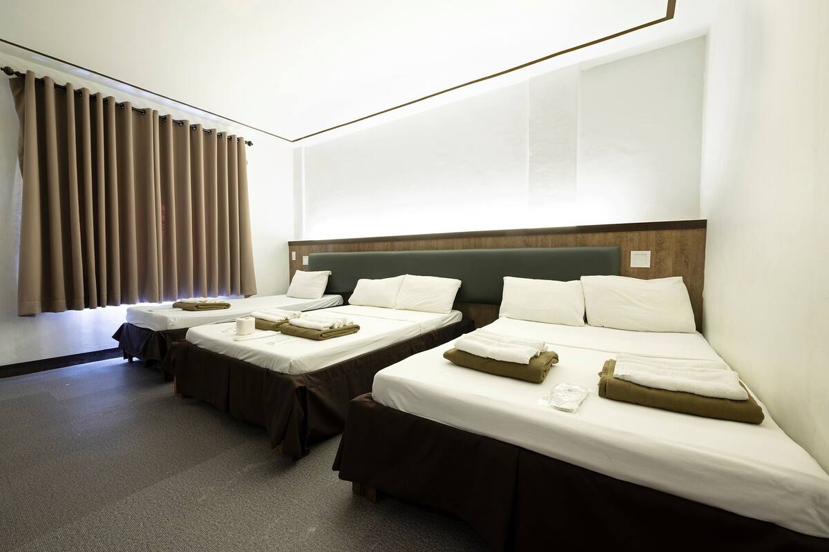 Habitación de hotel con dos camas individuales, un ventanal con cortinas y suelo alfombrado.
