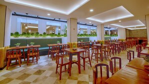 Un restaurant spacieux avec de hauts plafonds, des tables et des chaises en bois, et un mur végétal orné de plantes.