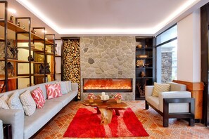 Un salon chaleureux avec une cheminée en pierre, un canapé, une table basse et une bibliothèque remplie d’objets décoratifs.
