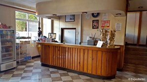 Un comptoir d’accueil avec un guichet d’enregistrement, un réfrigérateur et une fenêtre donnant sur un espace verdoyant.