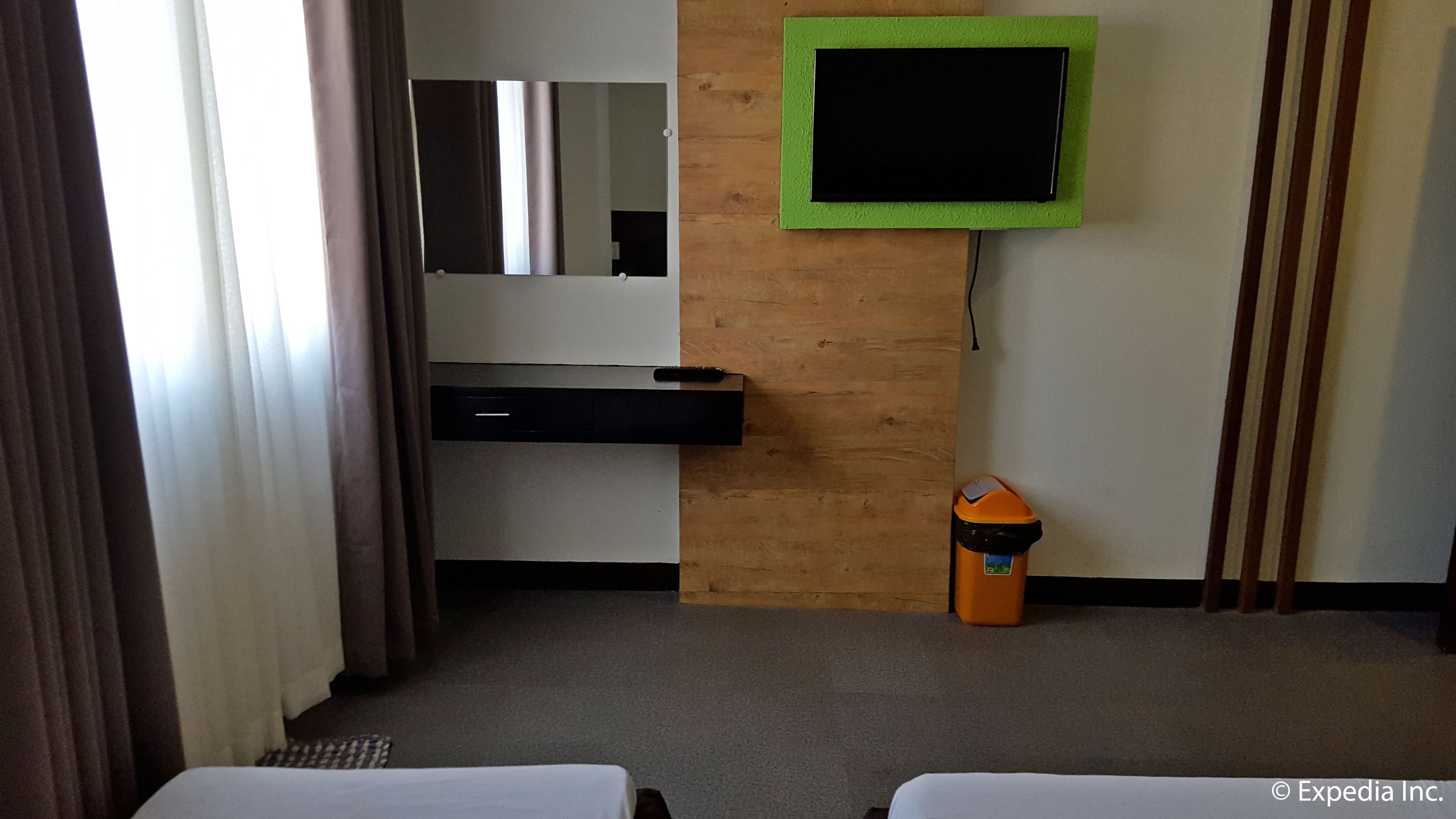 Habitación de hotel con cama, escritorio, espejo, televisor y cubo de basura.