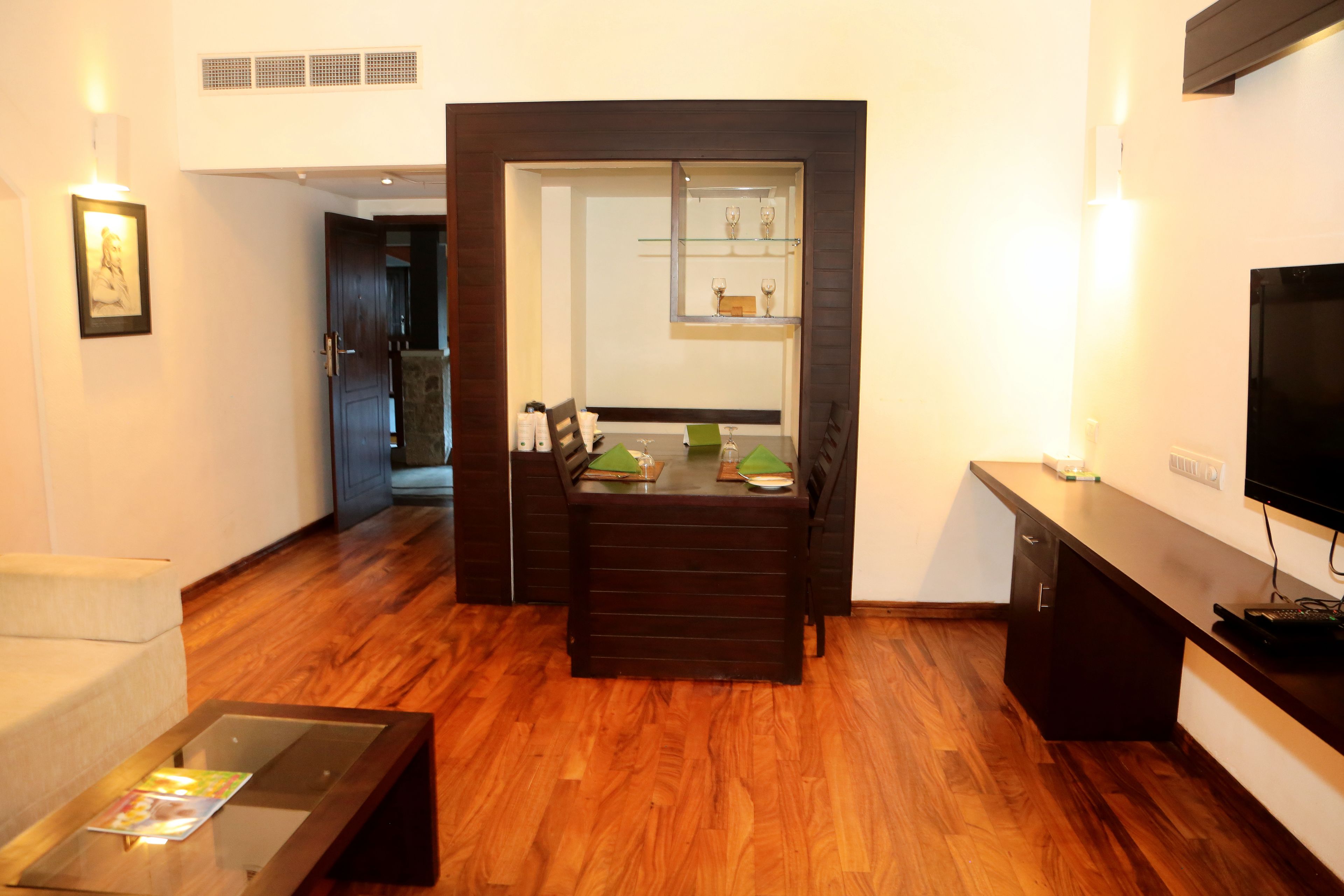A modern living room with a wooden floor, a glass coffee table, a sofa, a dining area with a table and chairs, and a TV on a stand.