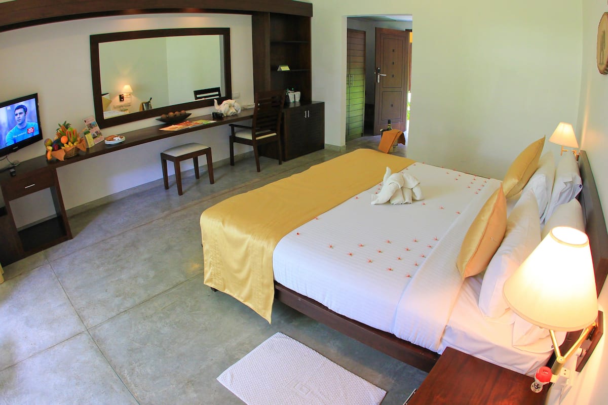 Habitación de hotel con cama, escritorio, silla, televisión y baño visible a través de una puerta abierta.