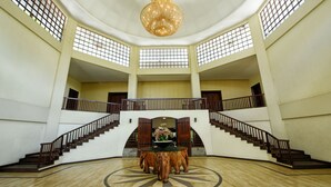 Un hall espacioso con una mesa redonda en el centro, una araña y una escalera con barandillas de madera.
